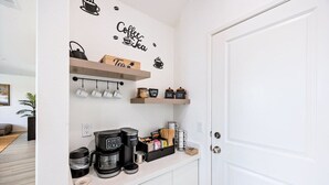 A kitchenette with a coffee machine, tea kettle, and tea mugs on the wall, and shelves with jars and containers.