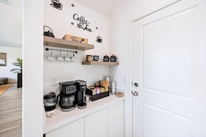 A kitchenette with a coffee machine, tea kettle, and tea mugs on the wall, and shelves with jars and containers. - Margaritaville | Pickleball, Pool+Spa, GameRoom! (Coachella)