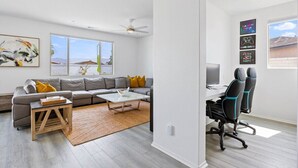 A modern living room with a grey sofa, a coffee table, and a desk with gaming chairs.
