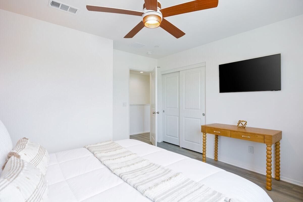Un dormitorio con cama, ventilador de techo, televisor y escritorio de madera.