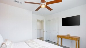 A bedroom with a bed, a ceiling fan, a TV, and a wooden desk.