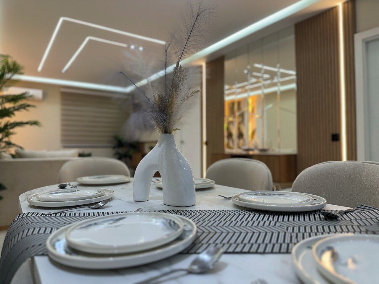 A dining table set with plates, cutlery, and a vase with dried plants.