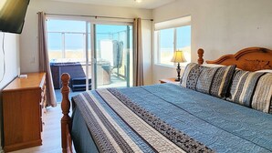 A bedroom with a bed, a wooden nightstand, a television, and a view of the beach. - Ocean Front on the Beach! Dog Friendly! (Waldport)