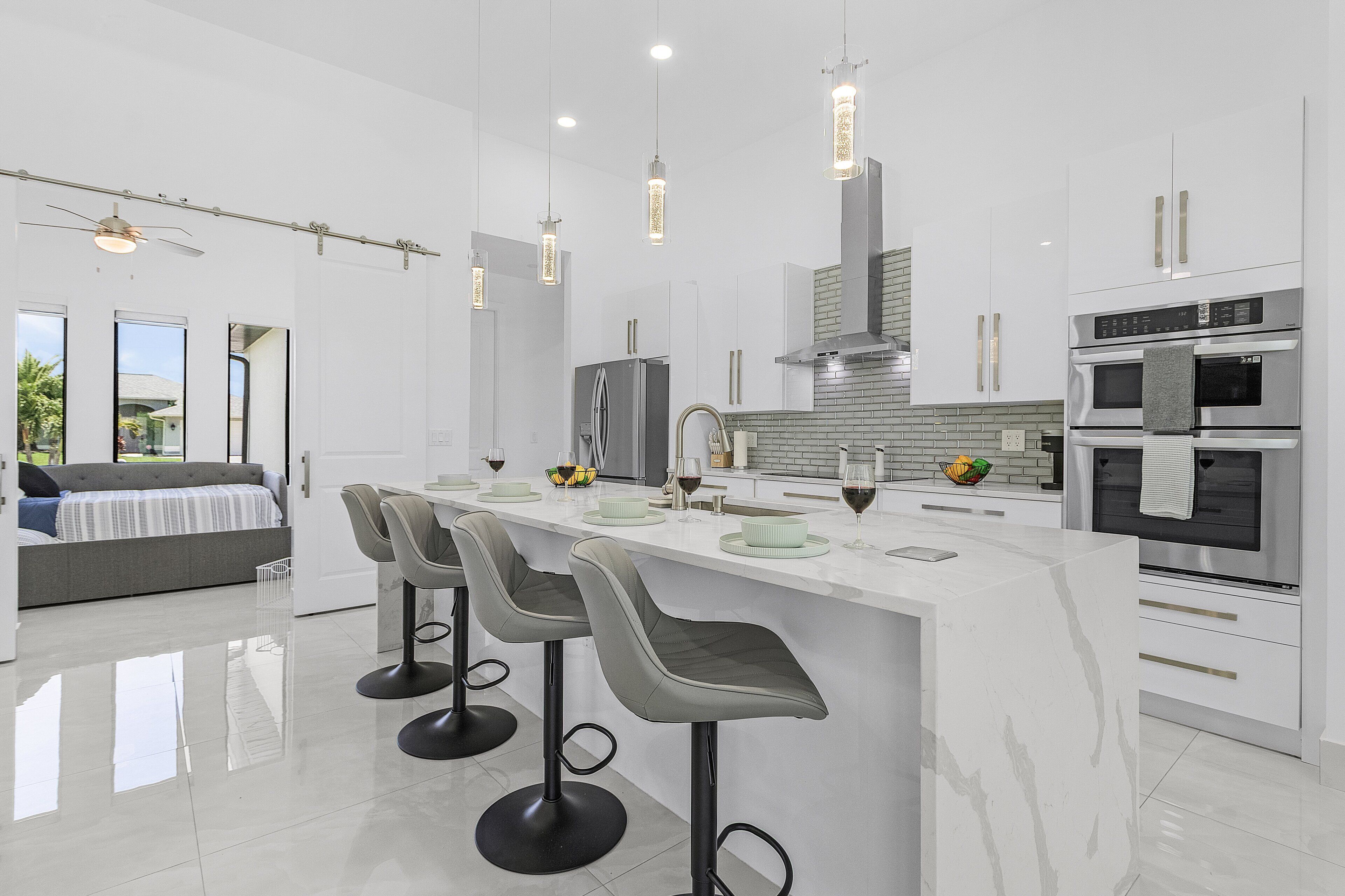 A modern kitchen with a central island, bar stools, stainless steel appliances, and a large window.