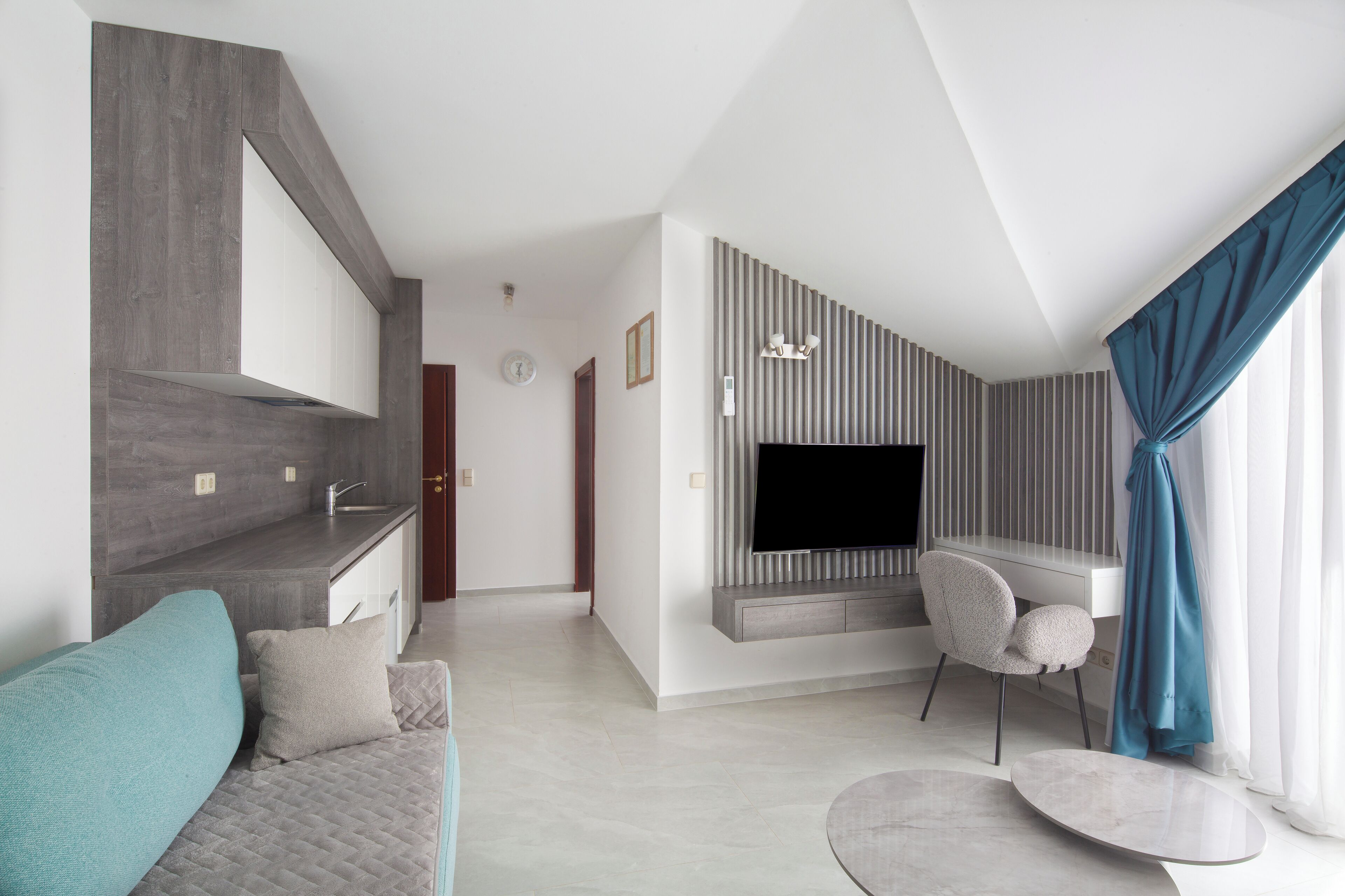 A modern living room with a grey sofa, a TV mounted on a wall, and a dining area with a table and chairs.