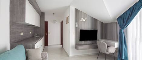 A modern living room with a grey sofa, a TV mounted on a wall, and a dining area with a table and chairs.