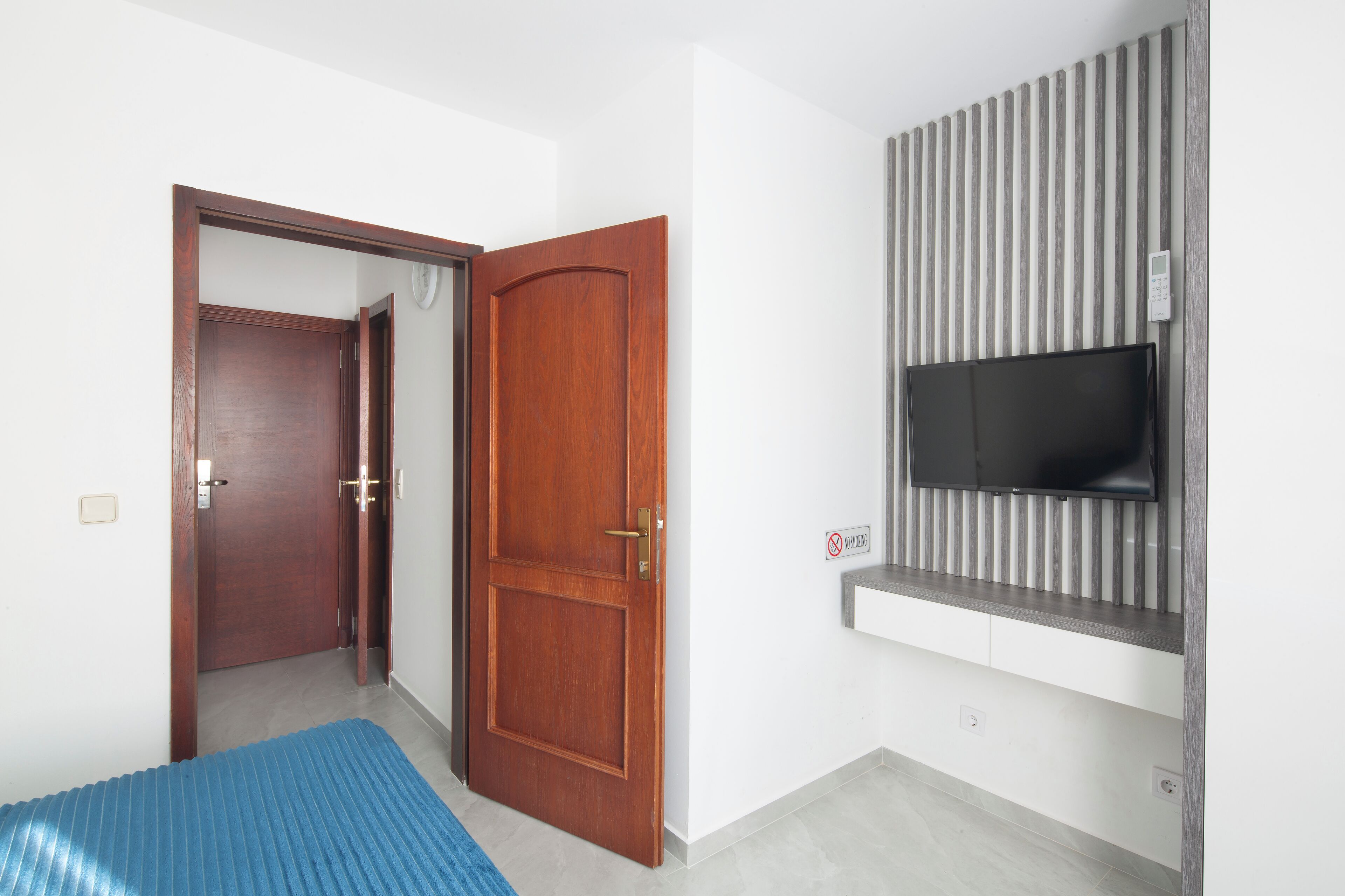 A room with a wooden door, a television mounted on a wall, and a blue mat on the floor.