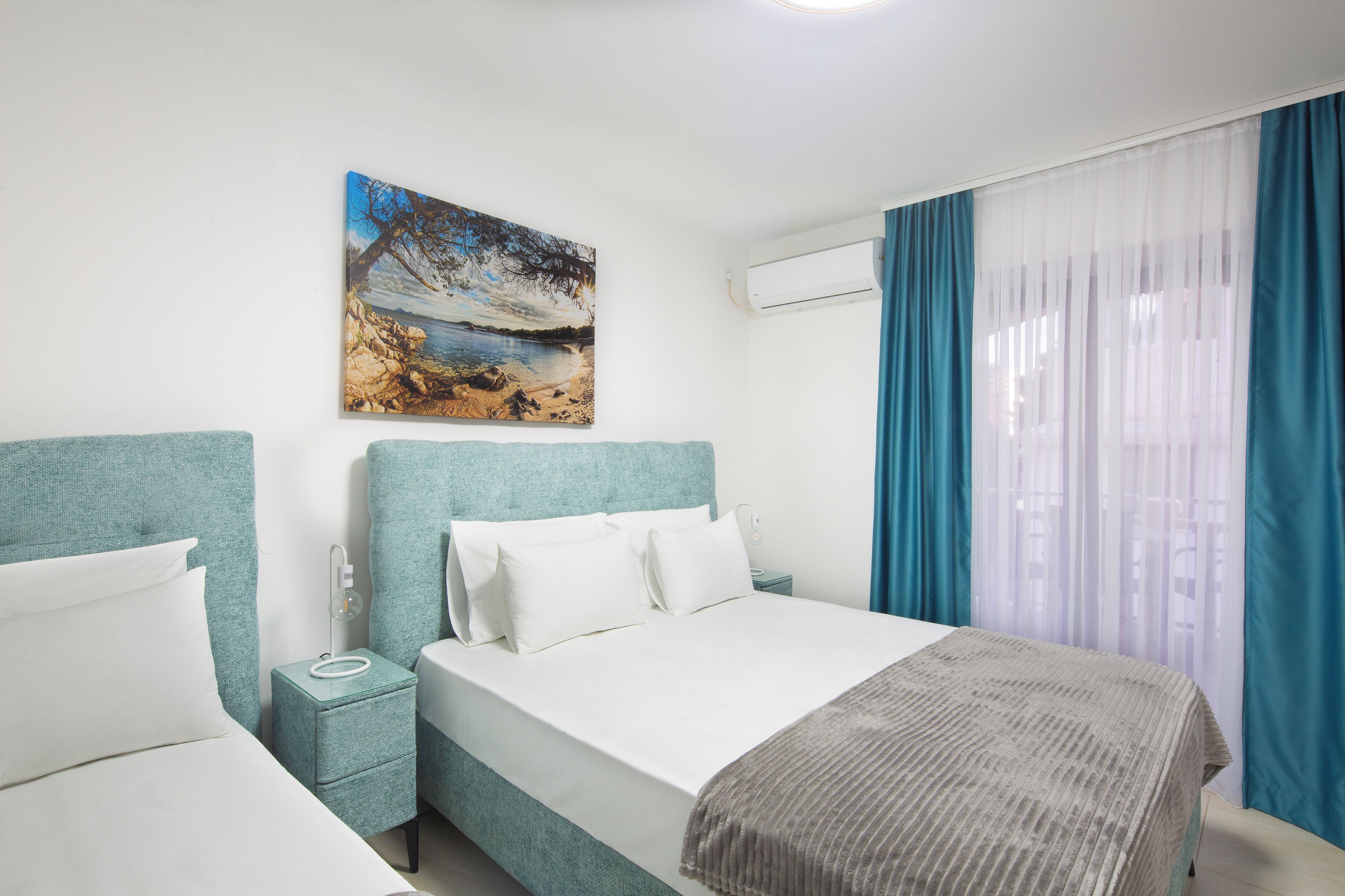 A hotel room with a bed, a nightstand, a painting, and a window with curtains.