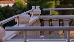 Un balcon avec une balustrade, deux tasses blanches et une vue sur de hauts immeubles et des arbres.