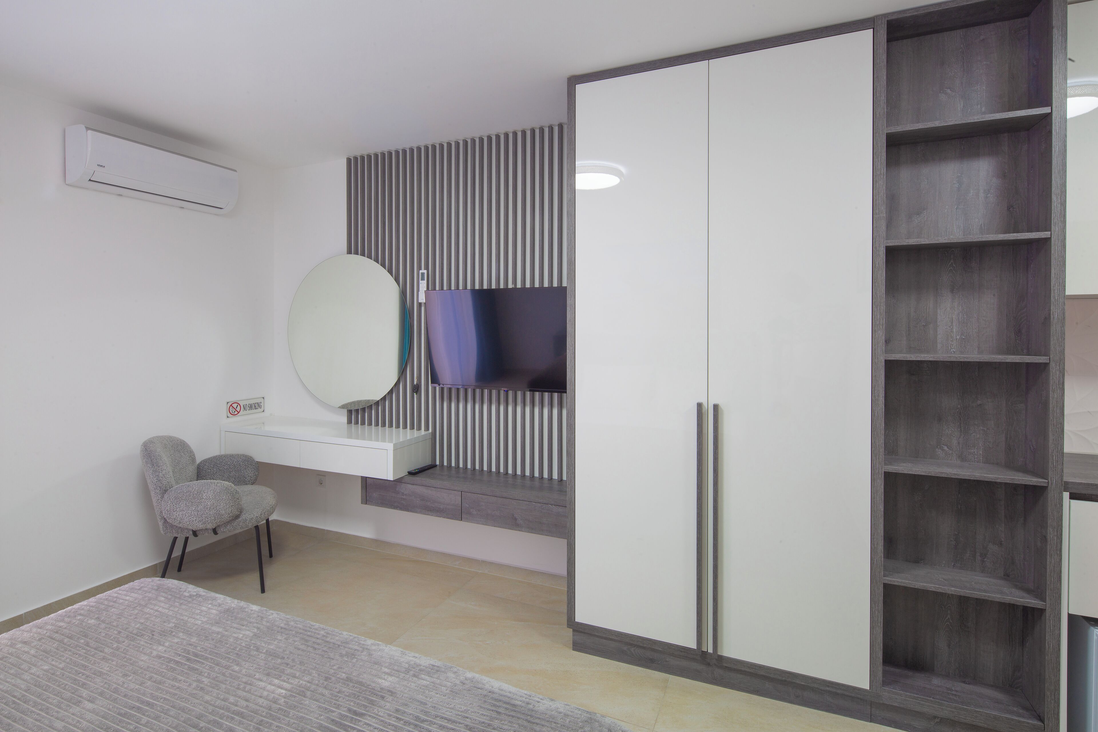 A modern bedroom with a bed, a vanity with a mirror, a chair, a wardrobe, and a TV.