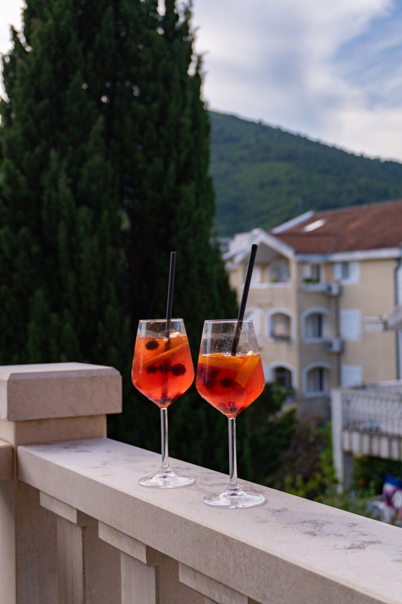 Zwei Cocktails auf einem Balkon mit Blick auf ein Gebäude und einen Baum.