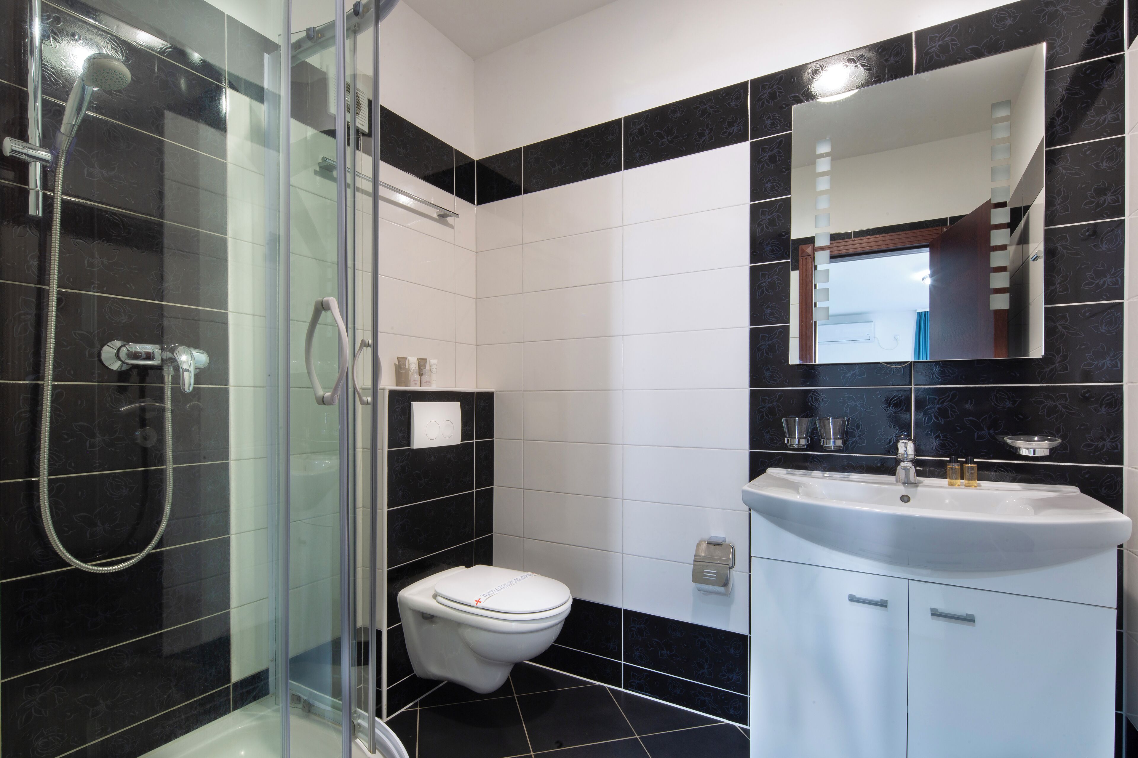 Un baño moderno con ducha compartimentada por vidrio, inodoro blanco y lavamanos con espejo arriba.