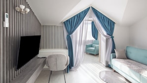 Un salon moderne avec un téléviseur à écran plat, un fauteuil gris, un canapé turquoise et une table basse ronde.