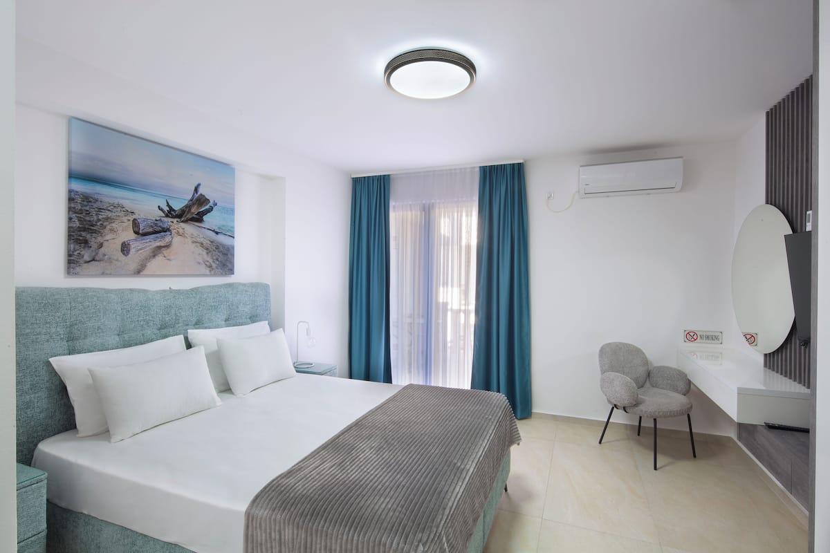 Une chambre d’hôtel avec un lit, un bureau, une chaise, un tableau et une fenêtre avec des rideaux.