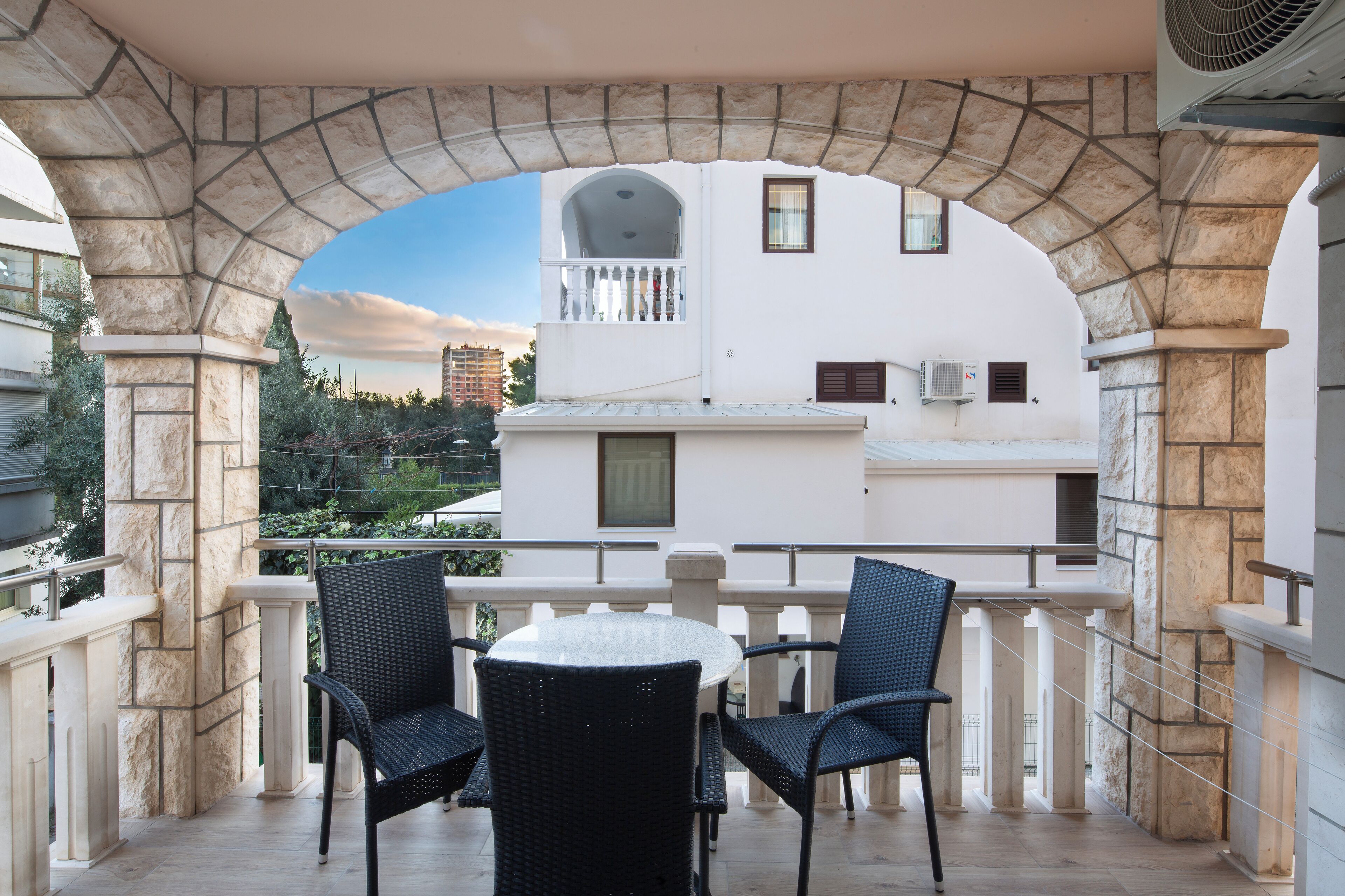 A balcony with stone columns, a round table, and two wicker chairs.