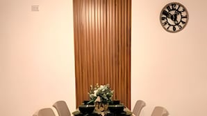A dining area with a rectangular table, four chairs, a wooden panel wall, and a wall clock. - Apartamento cerca a la playa Punta Roca (Puerto Colombia)