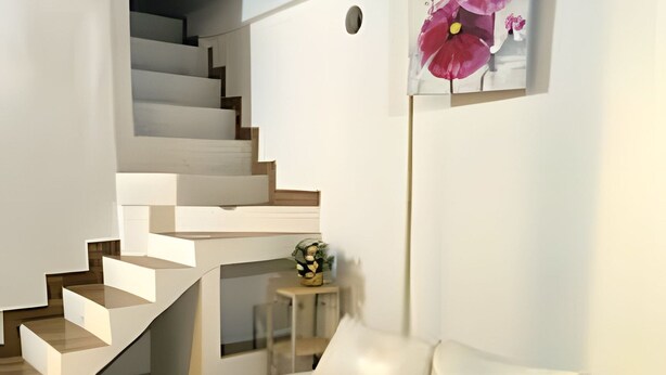 A modern interior with a staircase leading to a loft area, a white sofa, and a wall-mounted flower painting. - Apartamento cerca a la playa Punta Roca (Puerto Colombia)