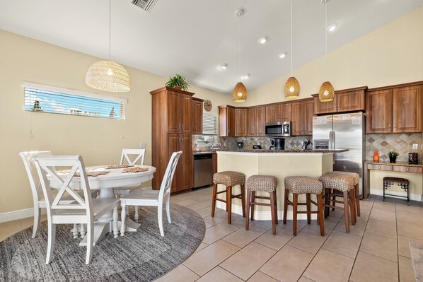 A kitchen with wooden cabinets, a central island, bar stools, and pendant lighting. - 3BR/2BA Home | Pool, Ping-Pong & Beach Nearby! (Fort Myers Beach)