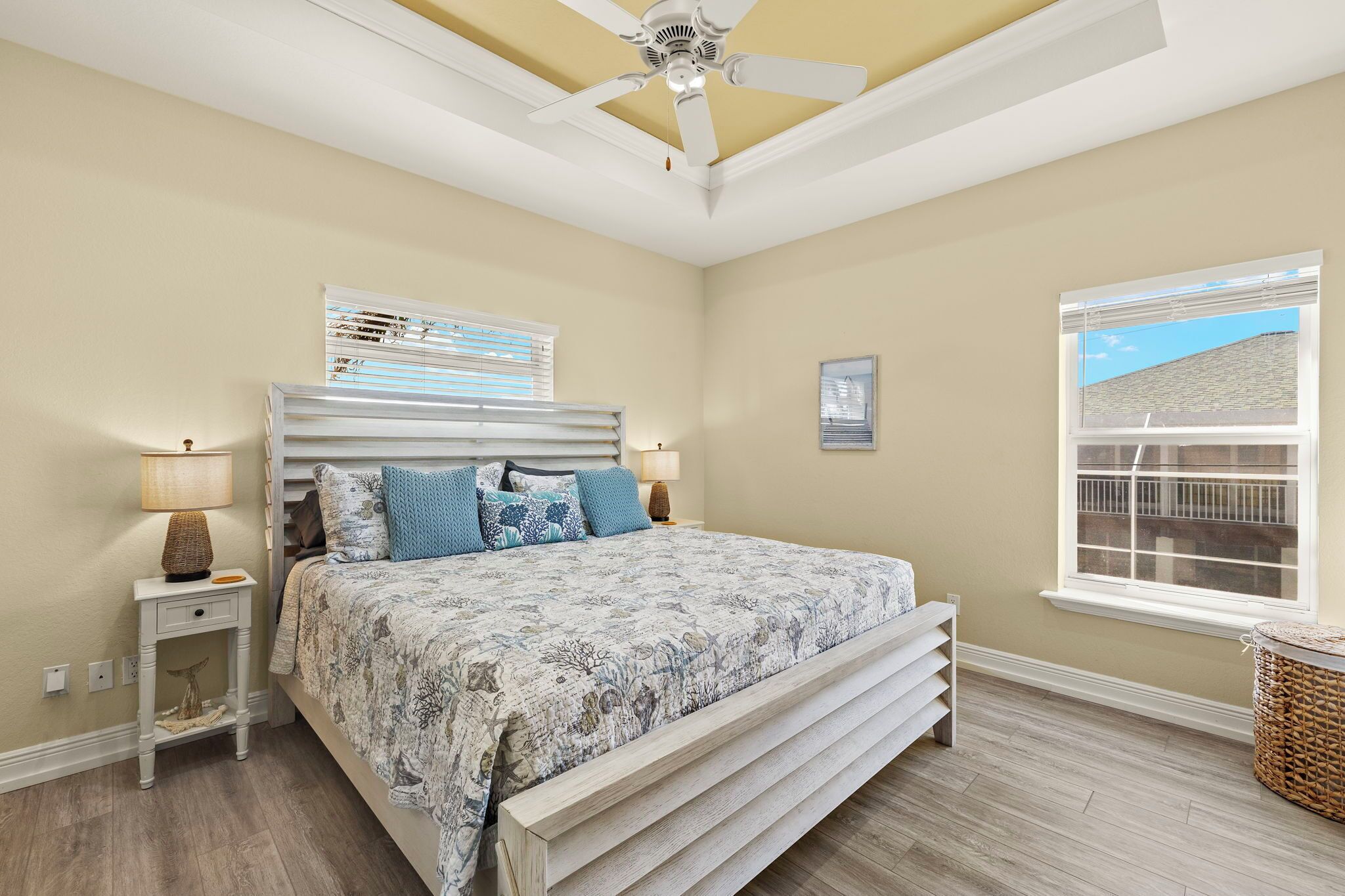 A bedroom with a bed, bedside lamps, a ceiling fan, a window, and a view of the outside.