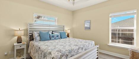 A bedroom with a bed, bedside lamps, a ceiling fan, a window, and a view of the outside.