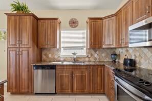 A kitchen with wooden cabinets, a stainless steel dishwasher, a built-in oven, and a window with blinds. - 3BR/2BA Home | Pool, Ping-Pong & Beach Nearby! (Fort Myers Beach)