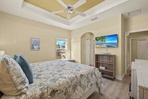A bedroom with a bed, a ceiling fan, a painting, and a wooden shelf. - 3BR/2BA Home | Pool, Ping-Pong & Beach Nearby! (Fort Myers Beach)