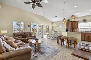 A spacious living room with a leather sofa, a coffee table, and a dining area with a kitchen in the background. - 3BR/2BA Home | Pool, Ping-Pong & Beach Nearby! (Fort Myers Beach)