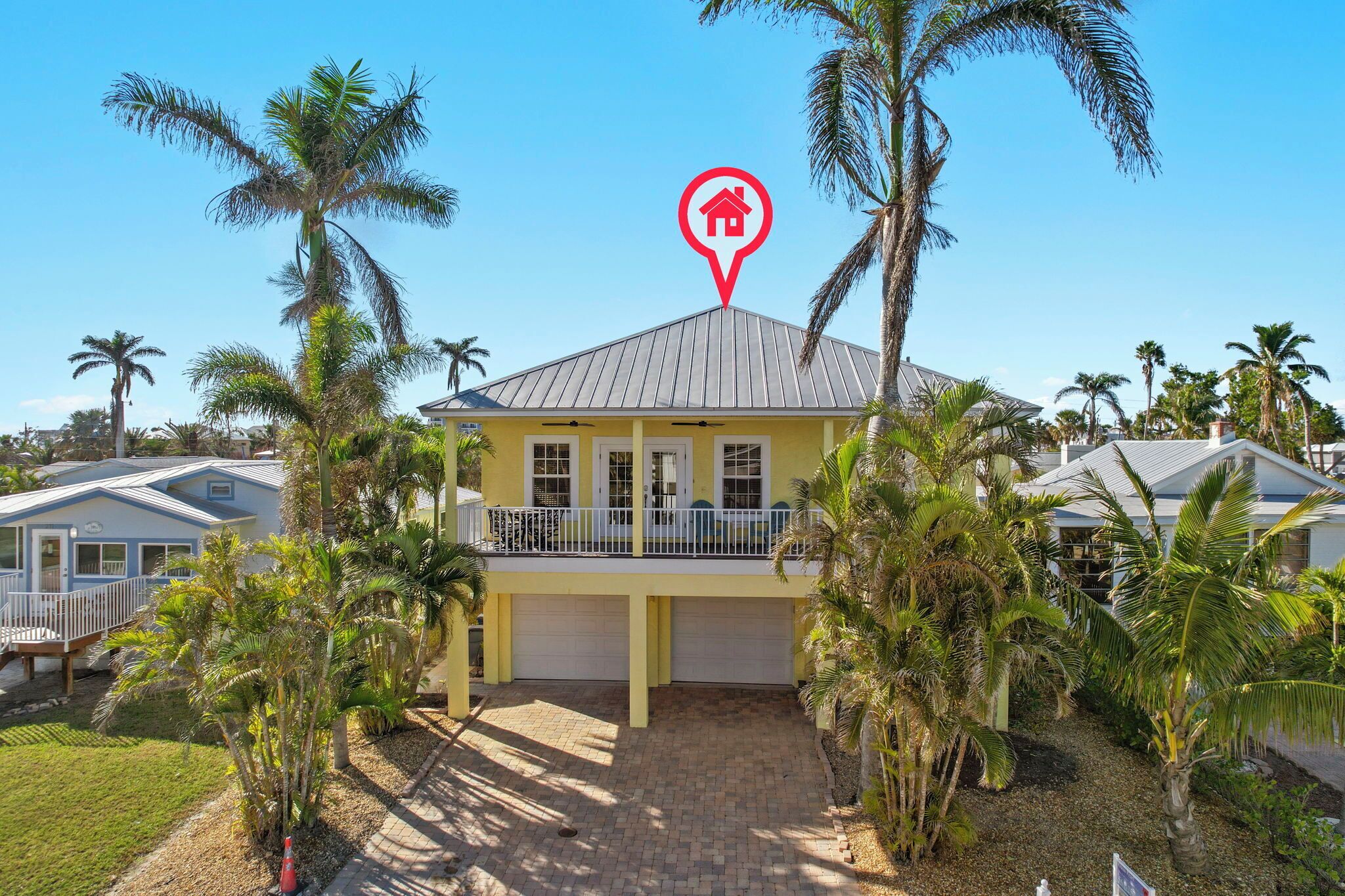 A two-story house with a balcony, surrounded by palm trees and a clear blue sky.