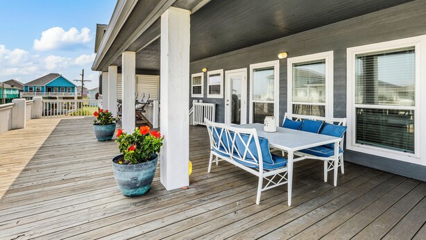 A covered outdoor deck with a table and chairs, potted plants, and a view of neighboring houses.