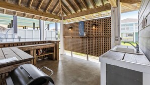 A covered outdoor area with a wooden table, a grill, and a sink.