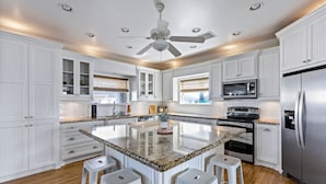 A spacious kitchen with white cabinetry, a central island with bar stools, a stainless steel refrigerator, and a ceiling fan.