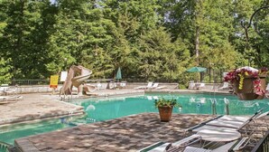 A swimming pool with lounge chairs and a slide, surrounded by trees.