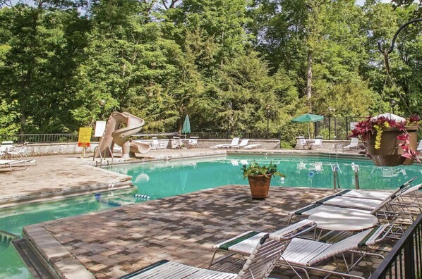 A swimming pool with lounge chairs and a slide, surrounded by trees. - Bearly Hidden: Peaceful Creekside Escape with Hot Tub (Gatlinburg)