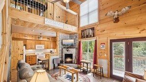 A spacious cabin with a loft bedroom, a fireplace, a dining area, and a kitchen.
