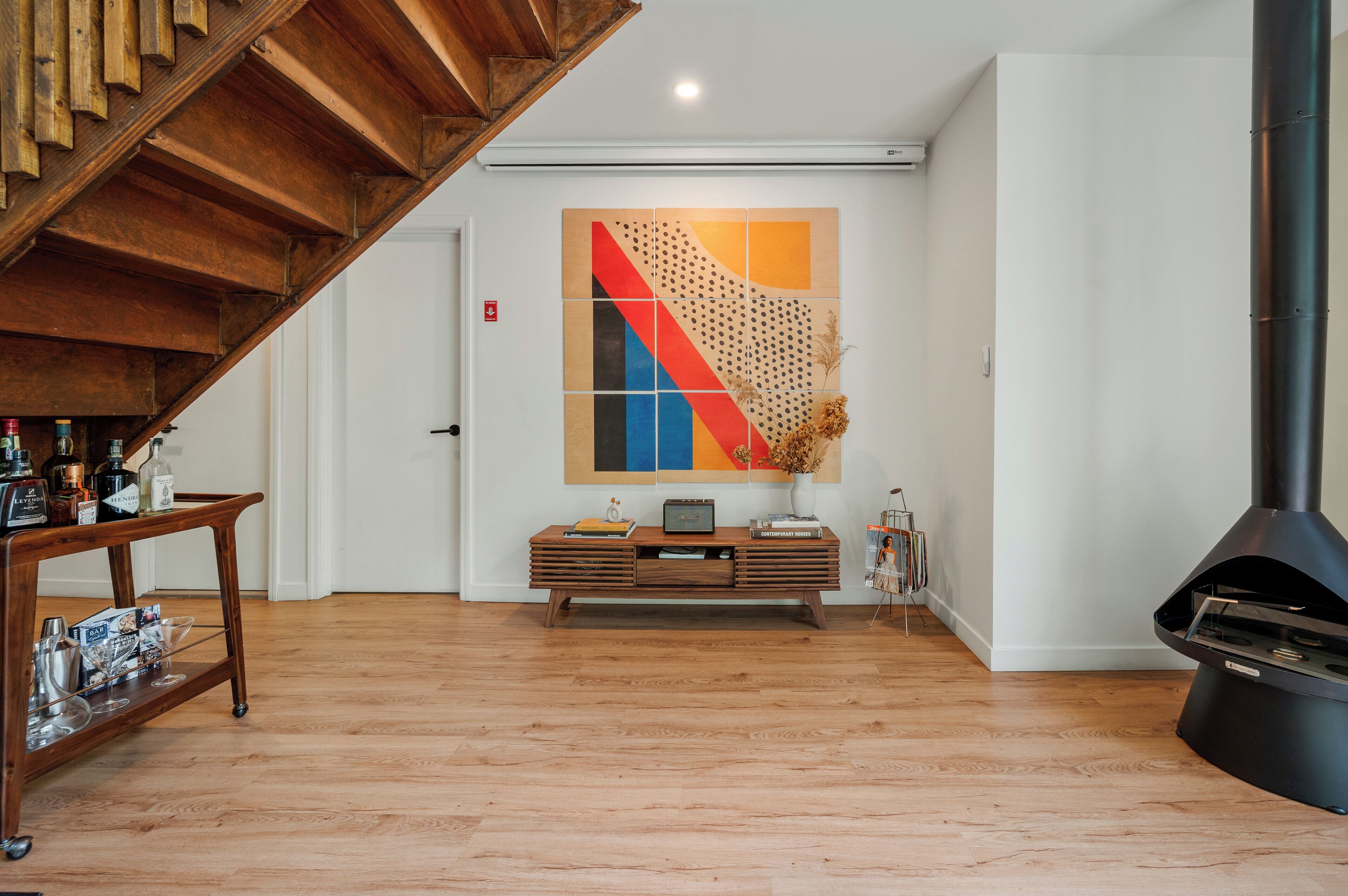 A spacious living area with a wooden staircase, a modern fireplace, and a colorful abstract painting on the wall.