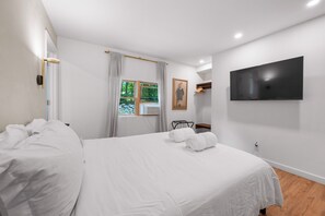 A hotel room with a large bed, a flat-screen TV mounted on the wall, and a window with curtains. - Modern Upstate Gem Surrounded by Trees with Hot Tub - 2.5 BD, 2 BH (Wallkill)