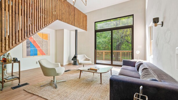 Un salon moderne avec un escalier en bois, une grande fenêtre donnant sur les arbres, un canapé et une table basse.