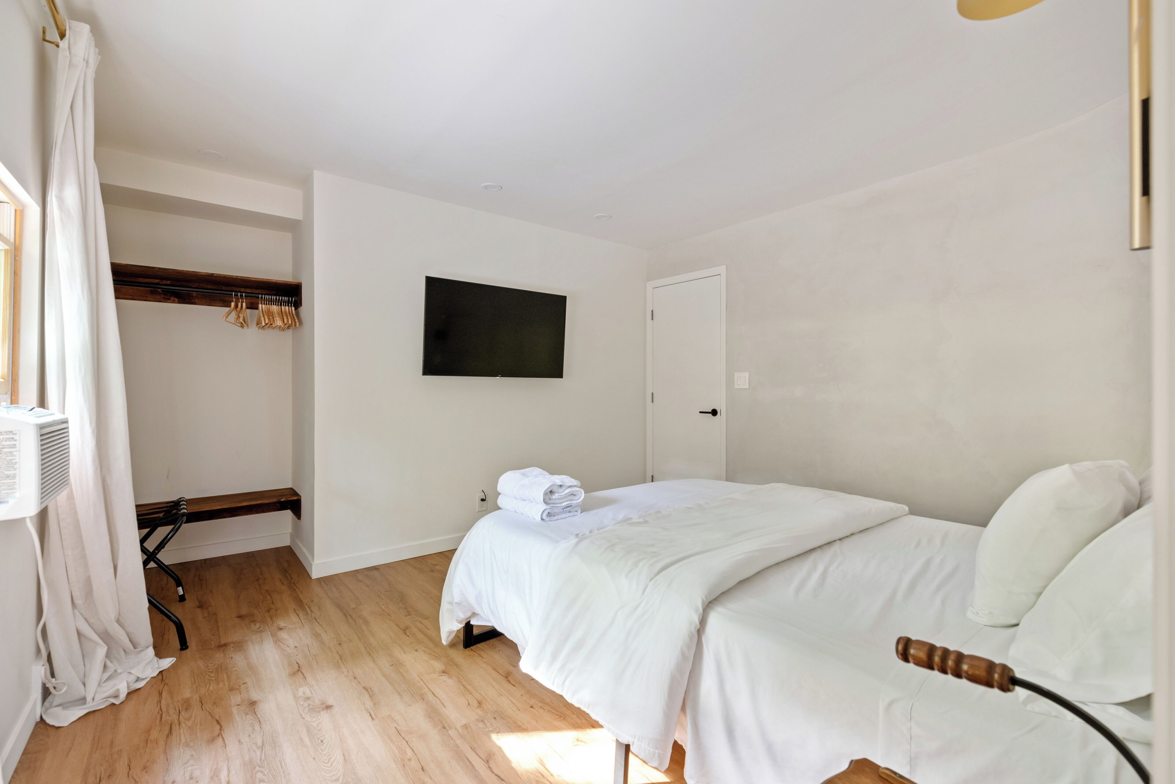 A bedroom with a bed, a television, a door, and a window with curtains.