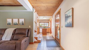 A modern living room with a brown leather sofa, wooden steps leading to a kitchen, and framed landscape pictures on the walls.