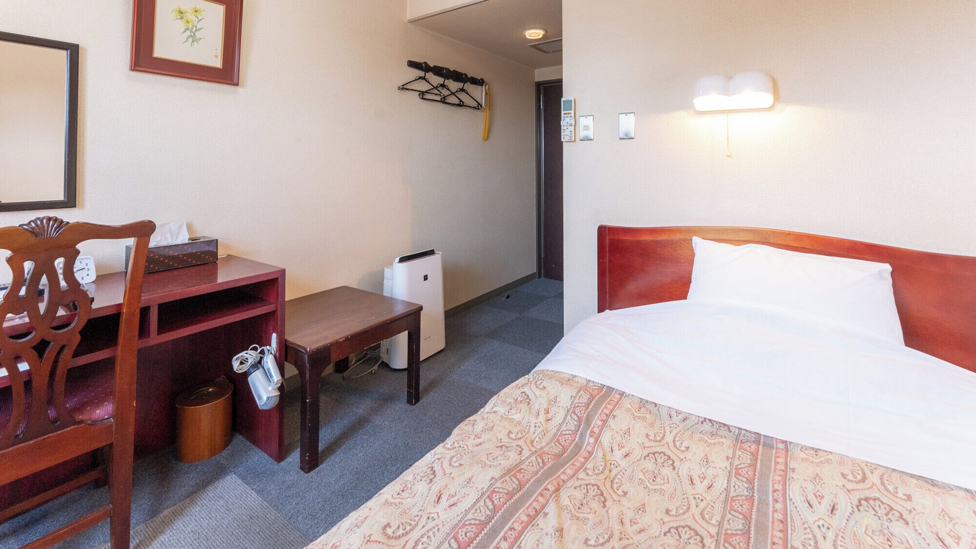 Une chambre d’hôtel équipée d’un lit, d’un bureau, d’une chaise, d’une poubelle et d’un luminaire fixé au mur.