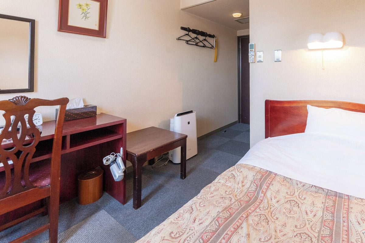 Ein Hotelzimmer mit einem Bett, einem Schreibtisch, einem Sessel, einem Mülleimer und einer Wandleuchte.