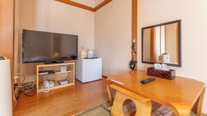 Habitación de hotel con techo de madera, un televisor de pantalla plana, un refrigerador pequeño, una mesita de noche con control remoto, una lámpara de noche y un espejo.