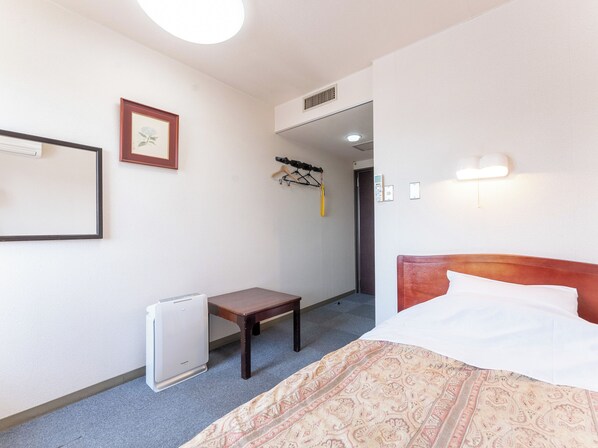 A hotel room with a bed, a small table, a heater, a coat rack, and a door leading to another room. - Omagari Empire Hotel (Daisen)