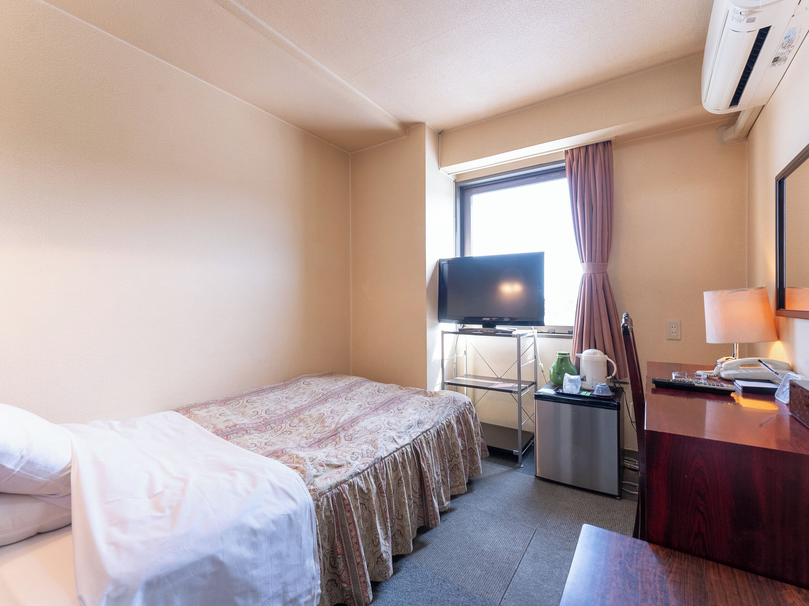 A hotel room with a bed, a desk with a television, a coffee maker, and a telephone.