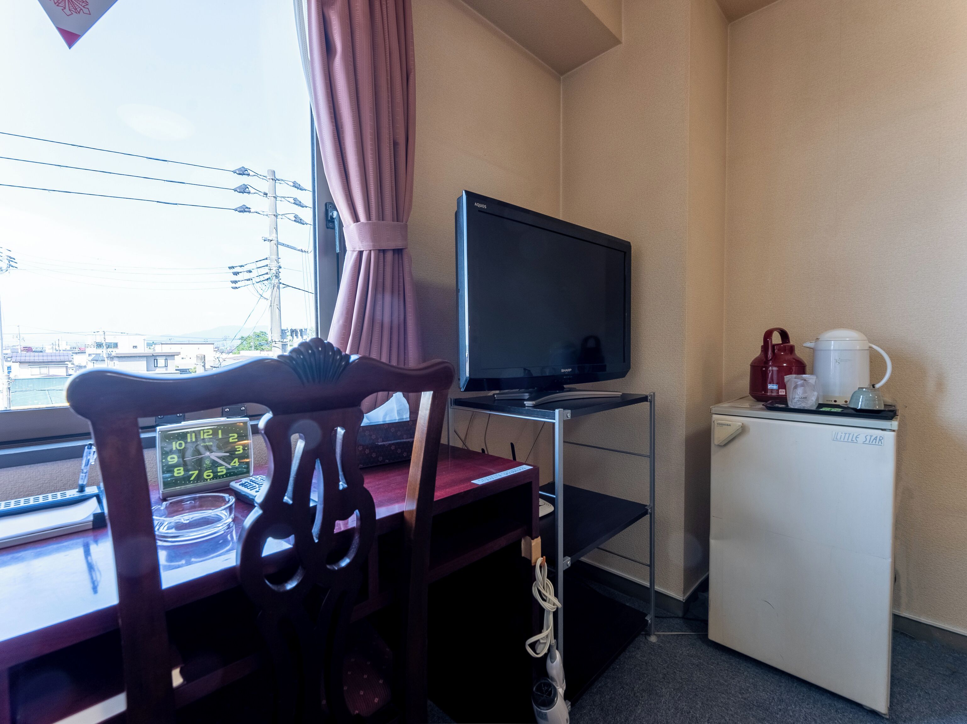 Ein Zimmer mit einem Holzbett, einem Fernseher auf einem Schrank, einem kleinen Kühlschrank und einem Fenster mit Vorhang.