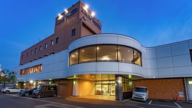 Un hotel moderno con fachada curva, ventanas amplias y un estacionamiento con varios coches.