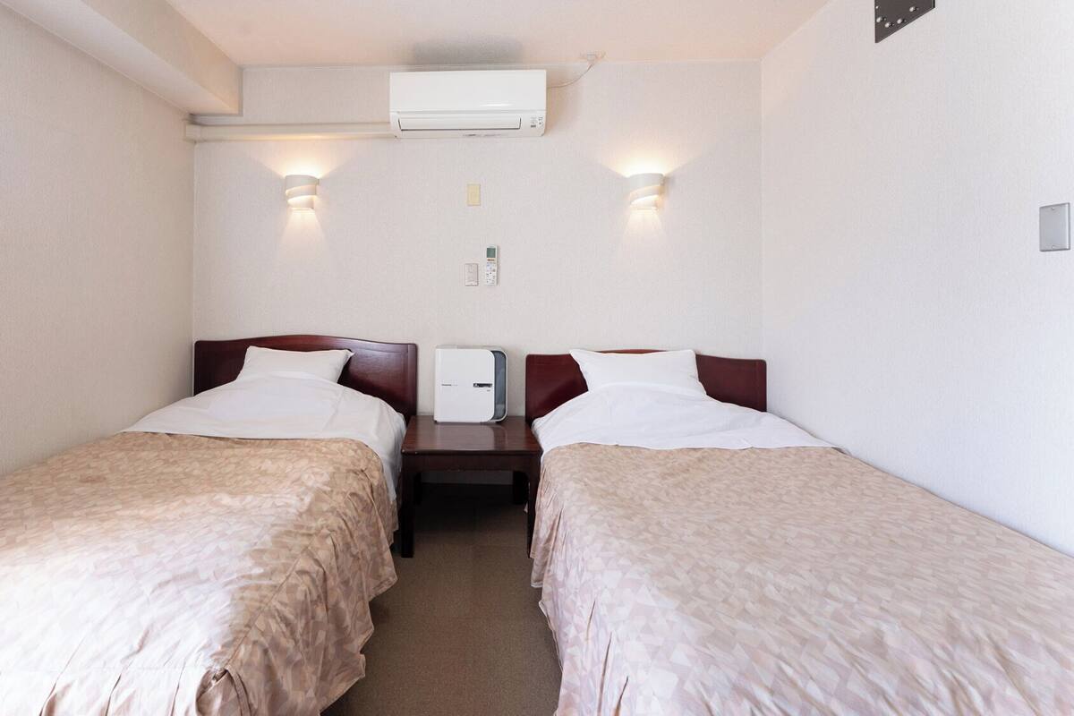 Ein Hotelzimmer mit zwei Einzelbetten, einer Wandklimaanlage und zwei Wandleuchten.