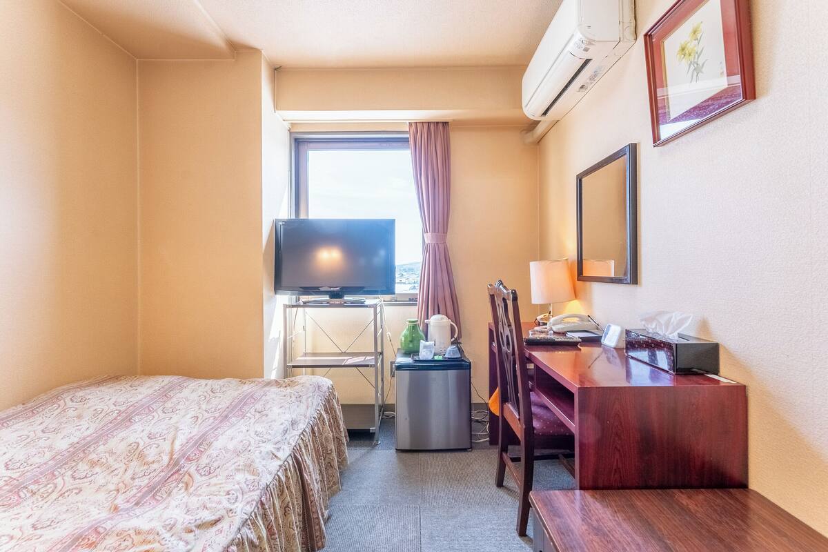 Ein Hotelzimmer mit einem Bett, einem Schreibtisch, einem Sessel, einem Fernseher und einem fenster mit Vorhängen.