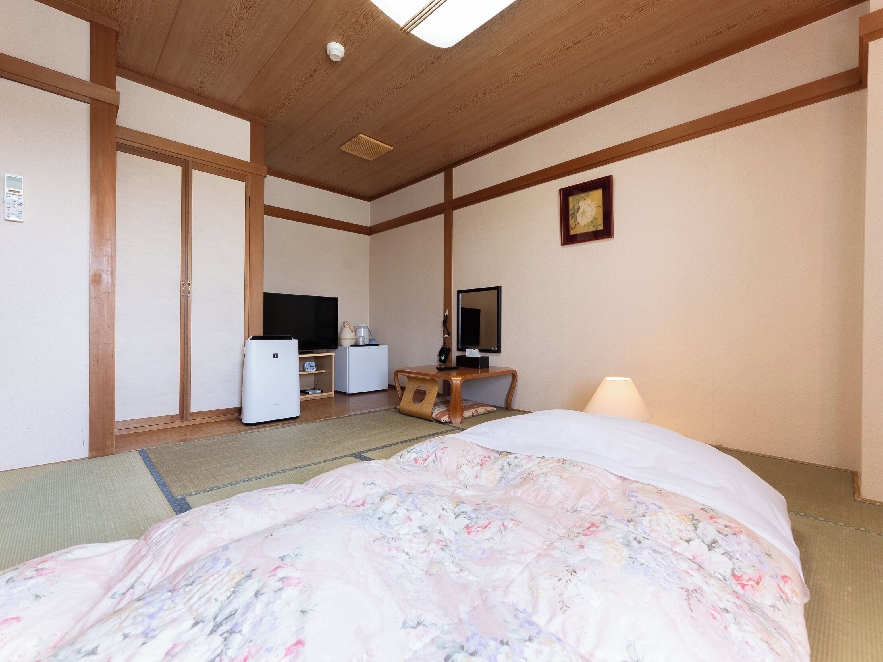 Hotelkamer met een bed, een televisie, een koelkast, een bureau met spiegel en een houten plafond.
