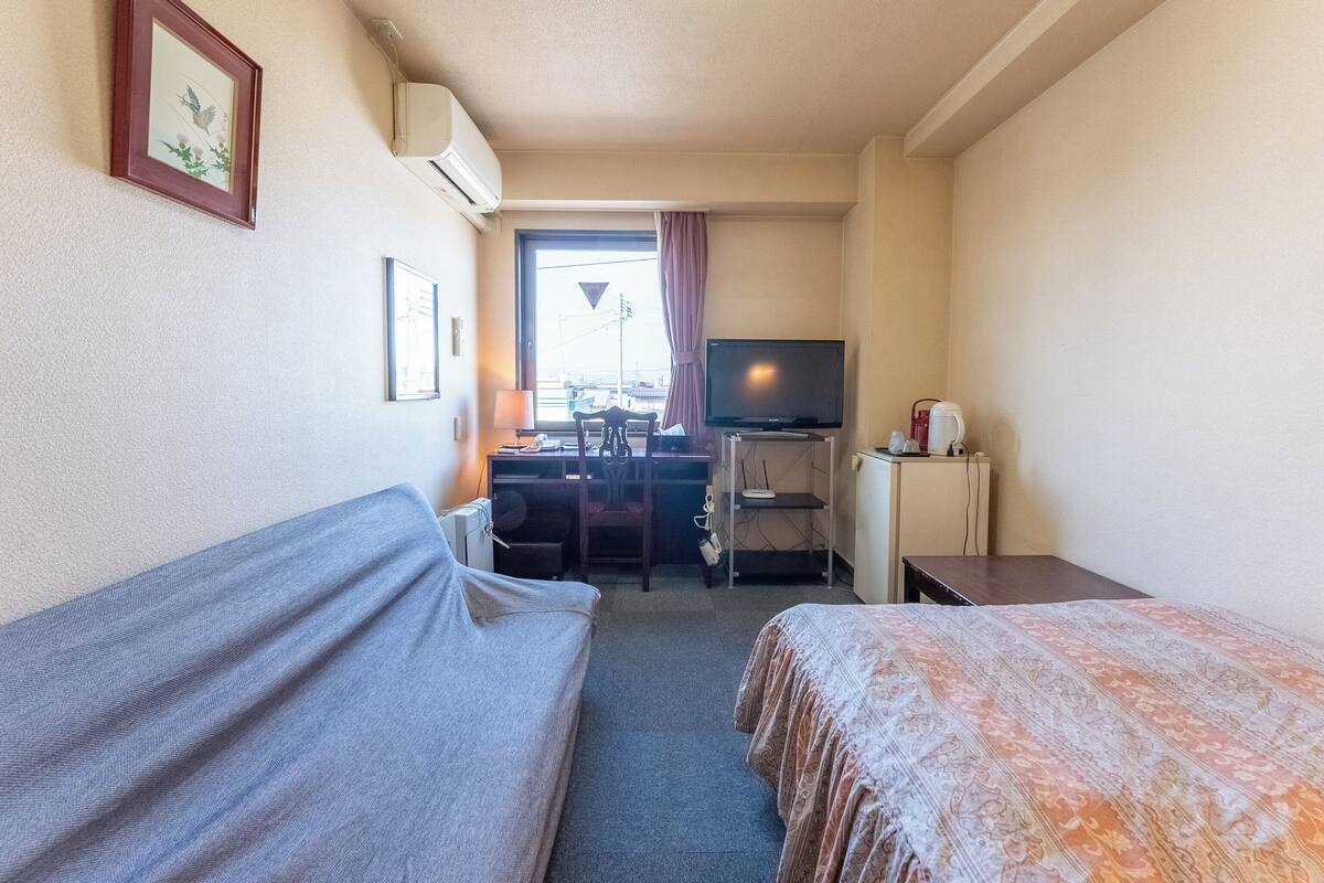 Ein Hotelzimmer mit Bett, Schreibtisch mit Computer, Fernseher und einer kleinen Küchenzeile.